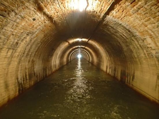 Tunnel voûté en pierre, traversé par un canal souterrain éclairé