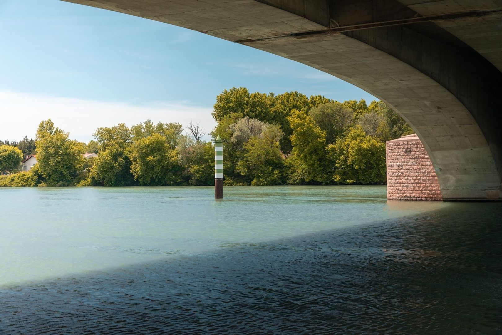 Balise fluviale rayée sous un pont, sur une large rivière navigable